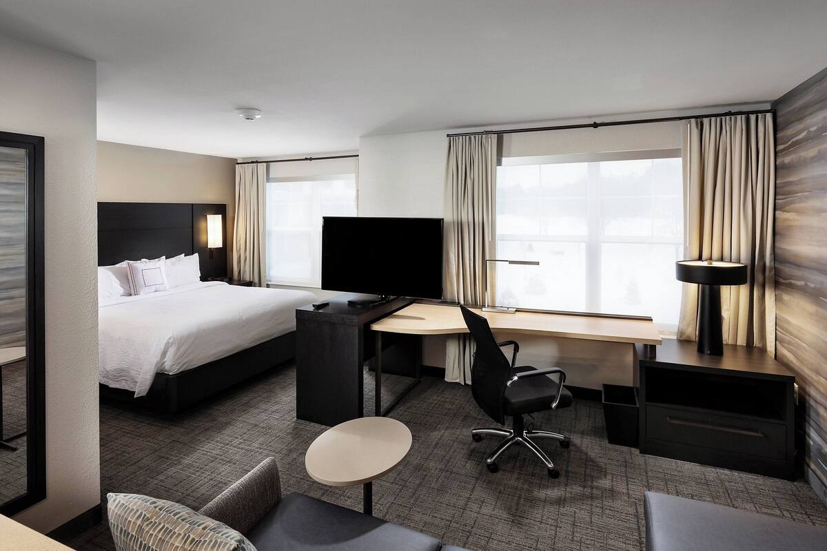 A hotel room with a bed, a desk, a chair, a TV, and a lamp.