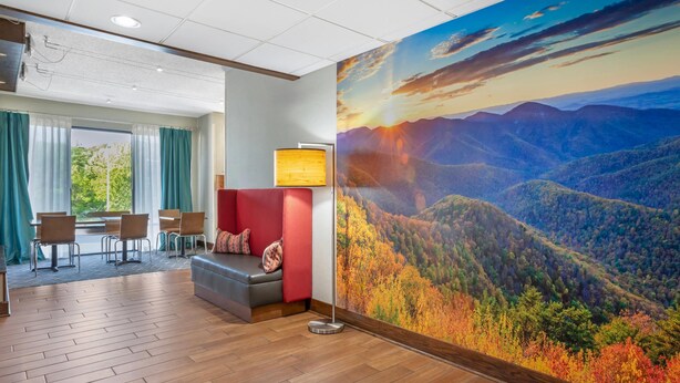 A hotel lobby with a large scenic wall mural, a seating area with a sofa and chairs, and a wooden floor. - Clarion Pointe Cherokee (Cherokee)