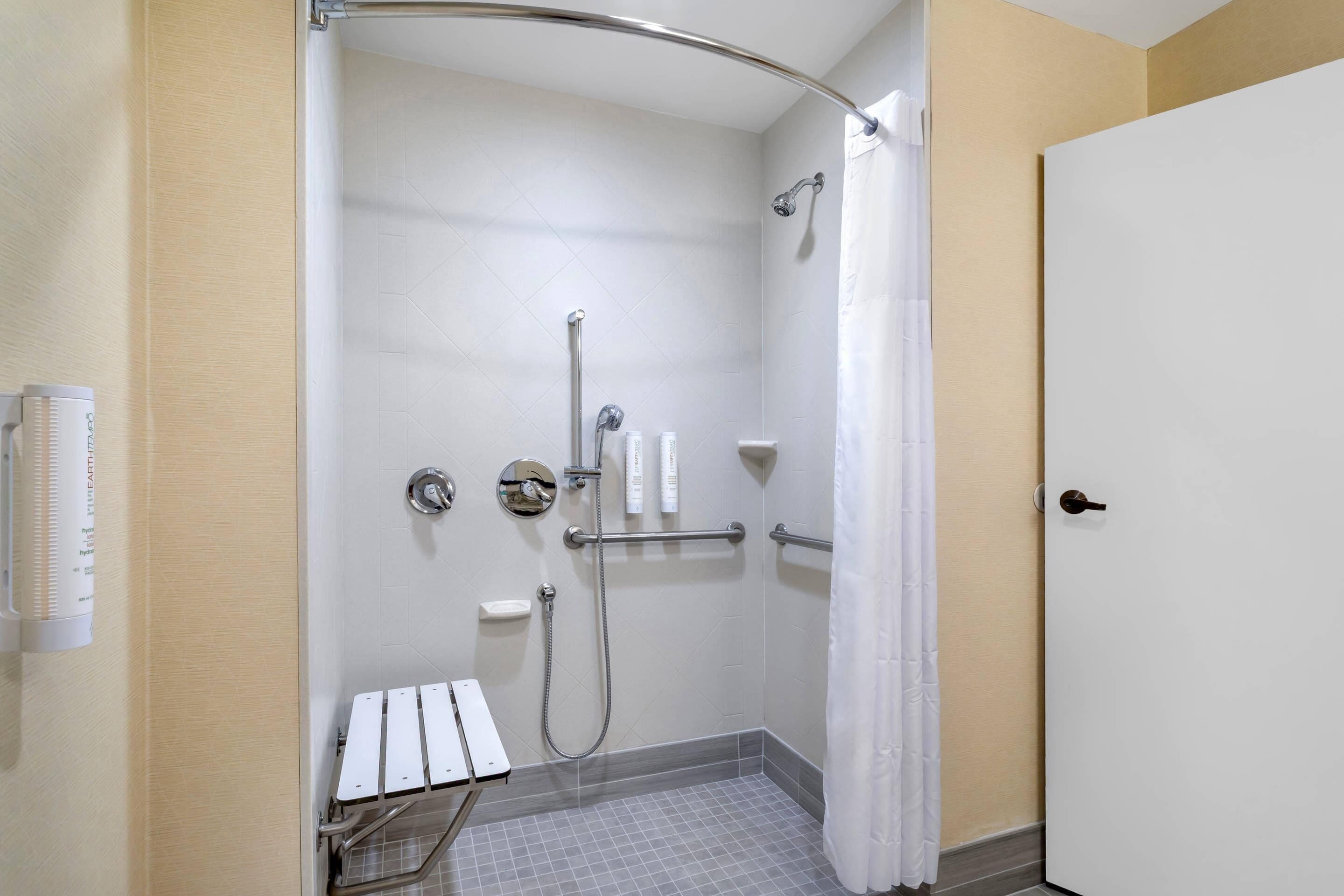 Un espace douche équipé d’une barre d’appui, d’une porte blanche et d’un porte-serviettes.