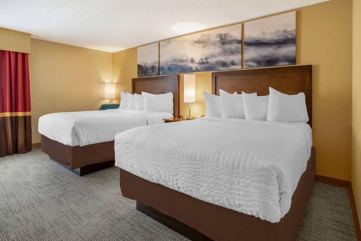 A hotel room with two beds, a red curtain, and a painting on the wall.