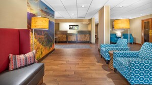 A lobby with a reception desk, a red sofa, patterned blue armchairs, and a wooden floor. - Clarion Pointe Cherokee (Cherokee)