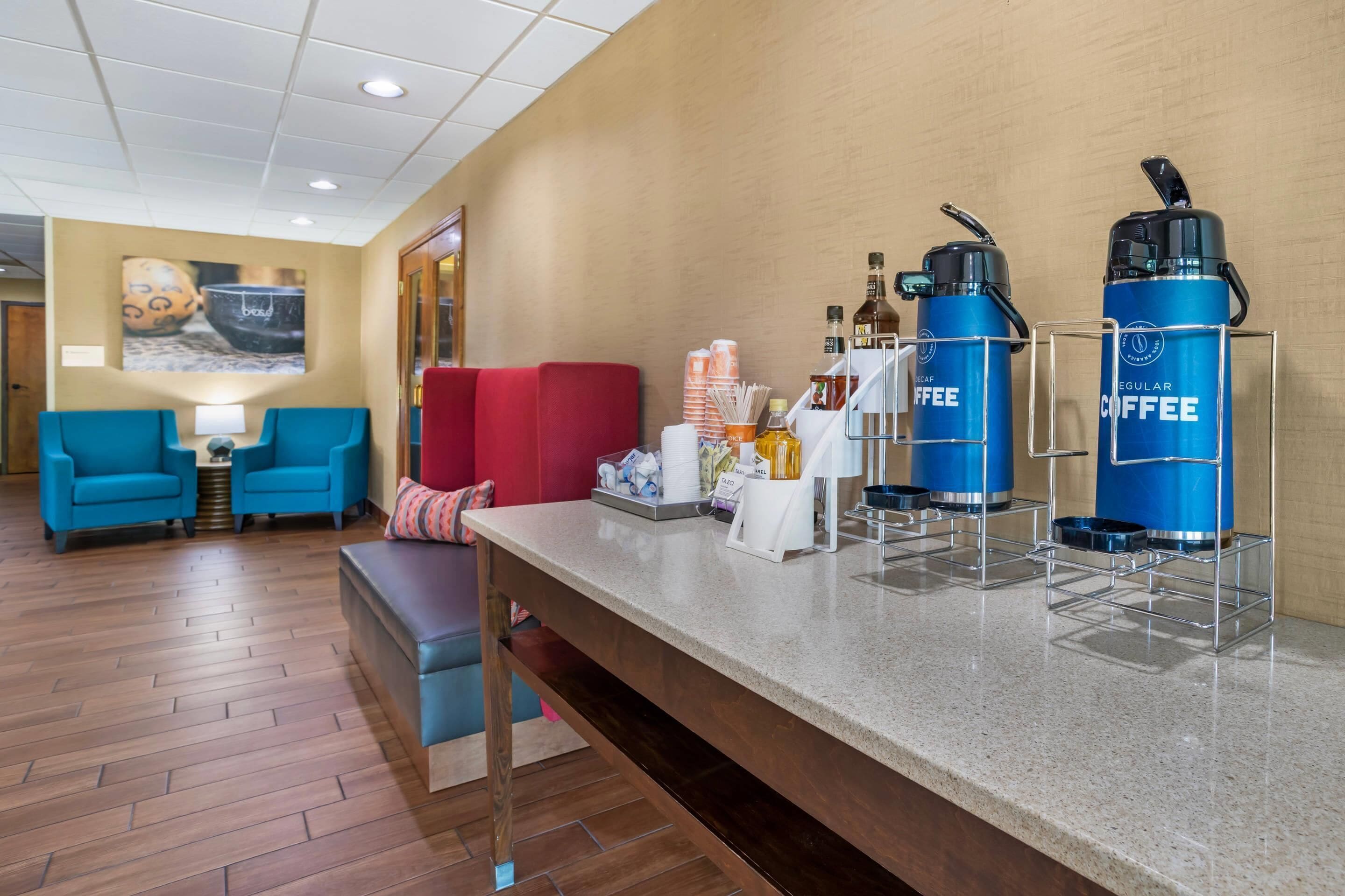 A hotel lobby with a coffee station, seating area, and a wall-mounted artwork.