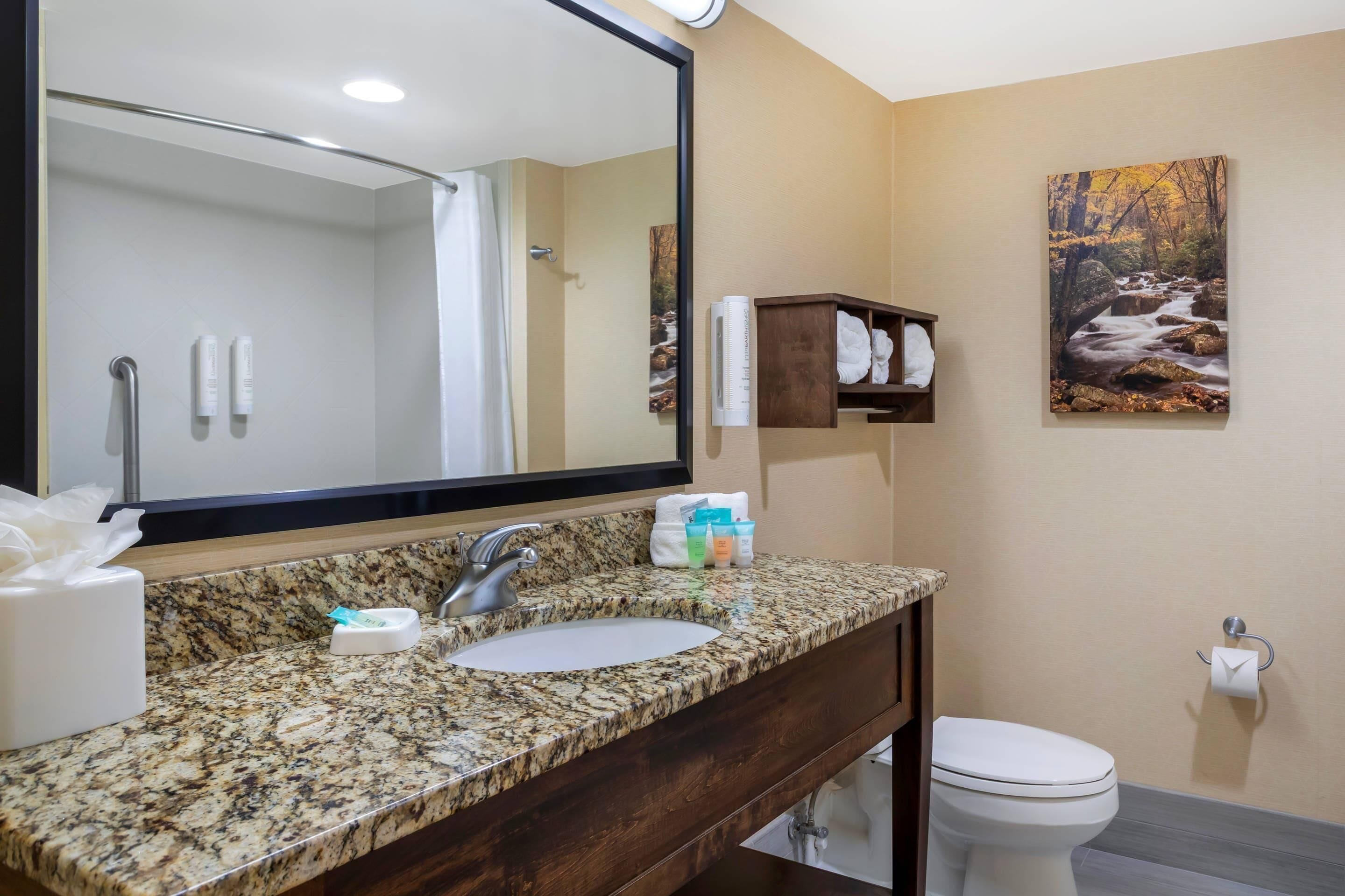 A bathroom with a granite countertop, a sink, a mirror, a towel rack, and a toilet.