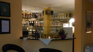 Un coin bar avec deux tabourets noirs, des étagères remplies de bouteilles et de verres, et une plante en pot posée sur le comptoir.
