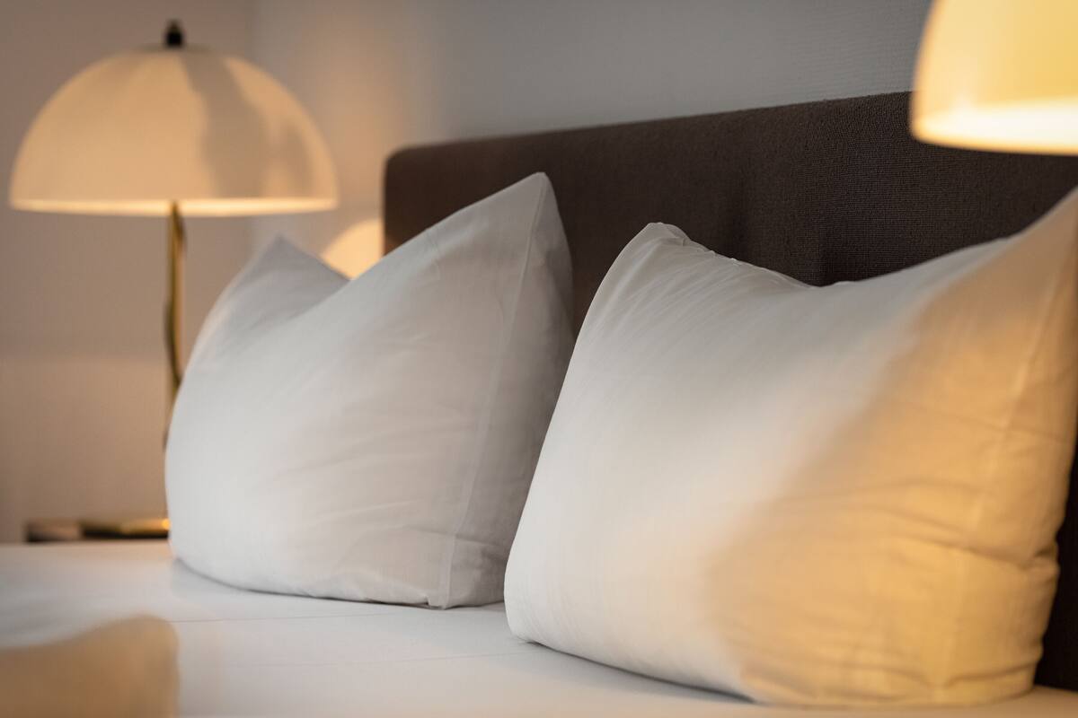 A neatly made bed with white pillows and a lamp in the background.
