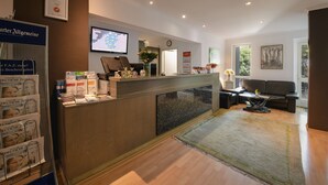 Un espace d’accueil comprenant un comptoir de réception, un ordinateur, une horloge et un coin salon avec un canapé et une table basse.