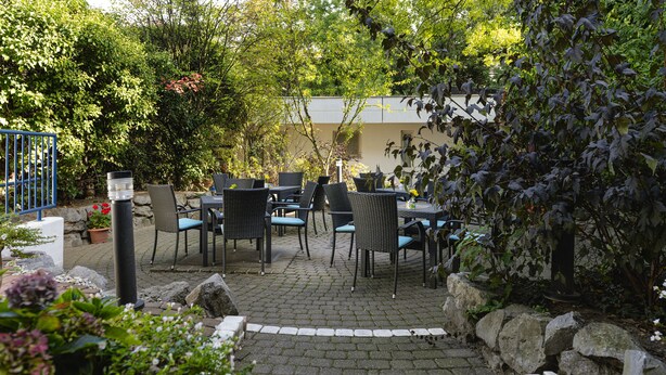 Un espace extérieur aménagé en terrasse, avec un sol en pierre, des meubles en osier et des plantes en pot.