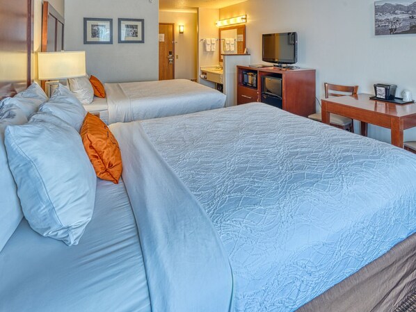Habitación de hotel con dos camas, un escritorio, un televisor y un baño visible a través de una puerta abierta.