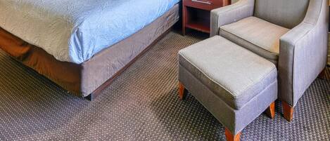 A hotel room with a large bed, a nightstand, a chair, and a lamp.