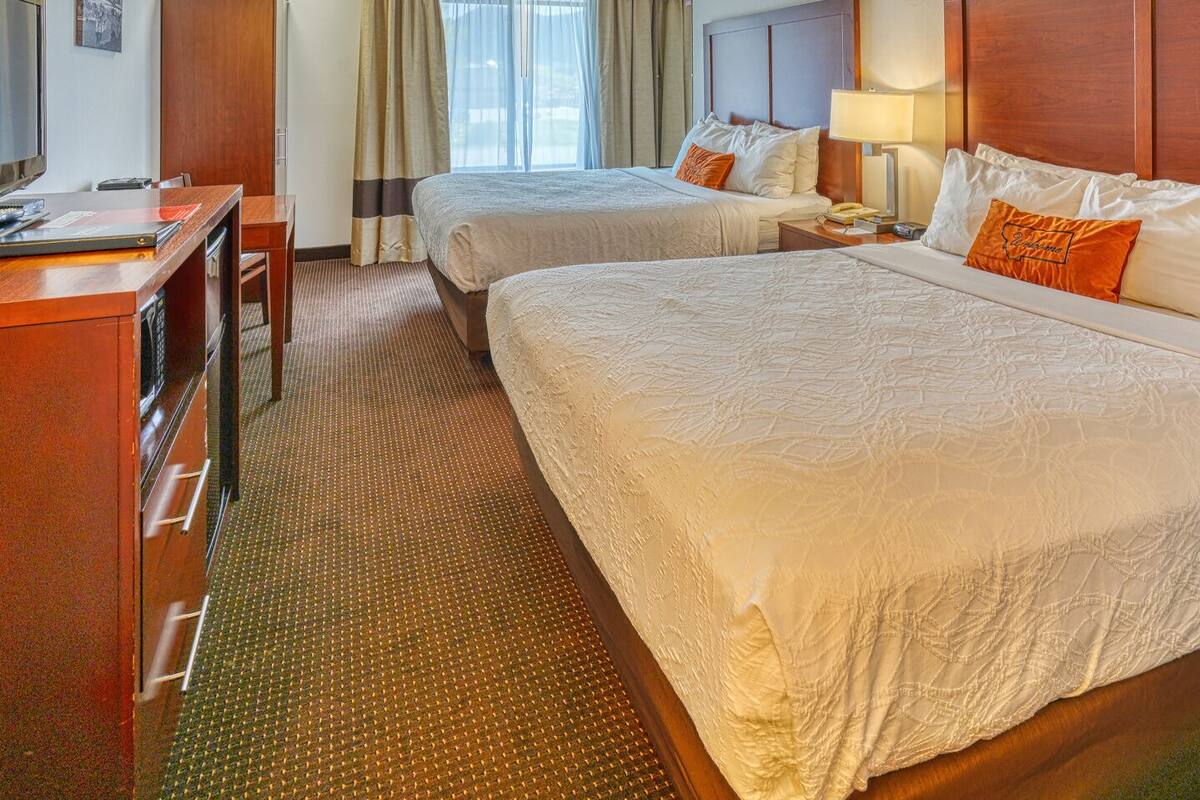 A hotel room with two beds, a desk, a chair, a television, and a window with curtains.