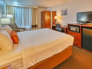 A hotel room with a large bed, a desk with a computer, a television, and a minibar.