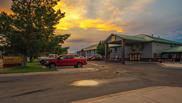 A hotel with a green roof, a signboard, and a parking lot with several vehicles.