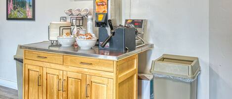 A kitchenette with a waffle maker, a trash bin, and a small stool.