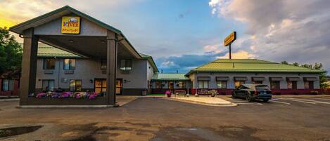 A motel with a covered parking area, a green-roofed building, and a sign indicating it is a 'Riverview Inn & Suites'.