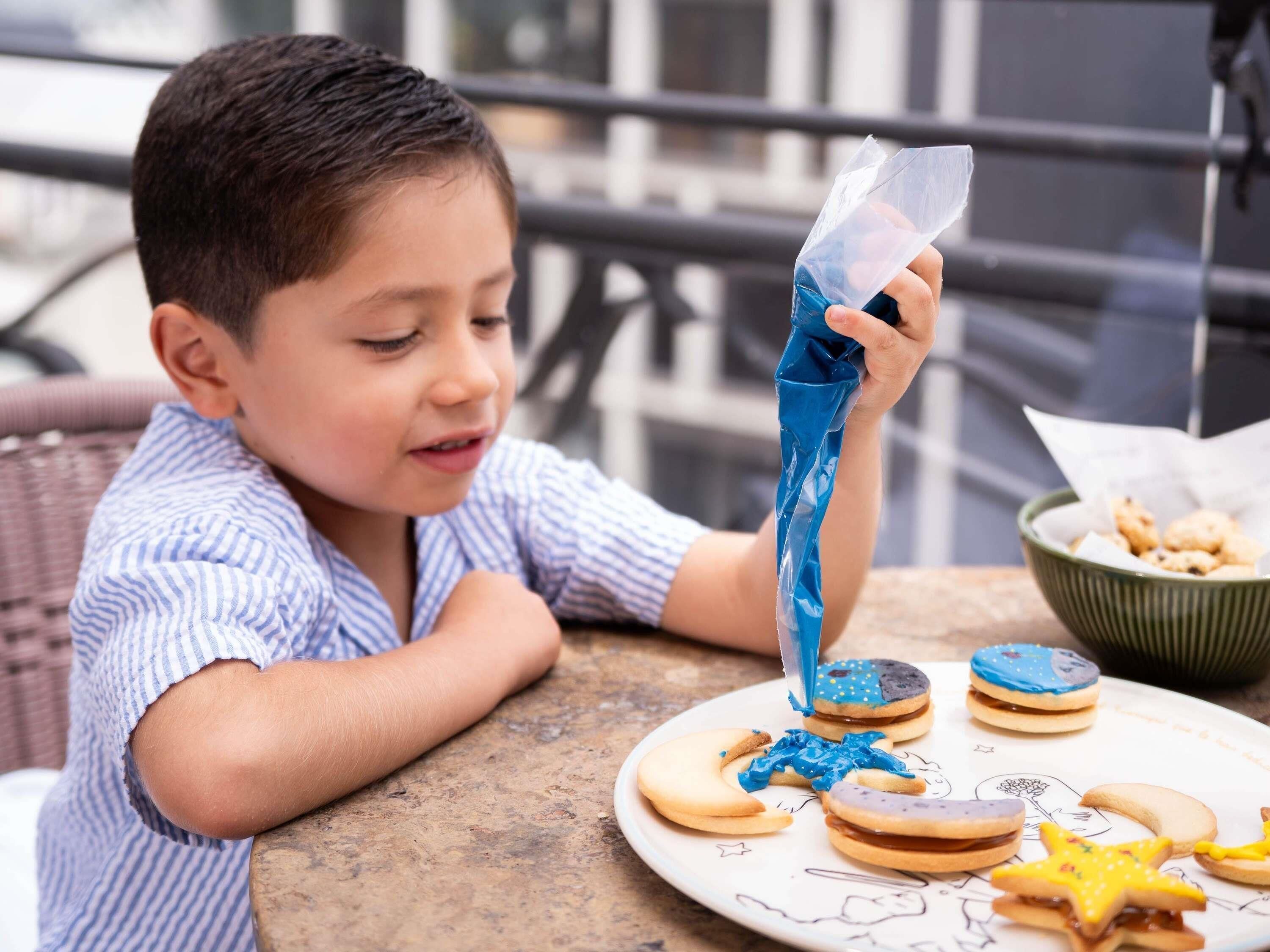 Un niño sentado a la mesa con un plato de galletas decoradas y un tazón de bocadillos.