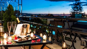 A balcony table set with a bottle of champagne, glasses, candles, and a tray with chocolates, overlooking a cityscape at dusk. - Sofitel Bogota Victoria Regia (Bogotá)