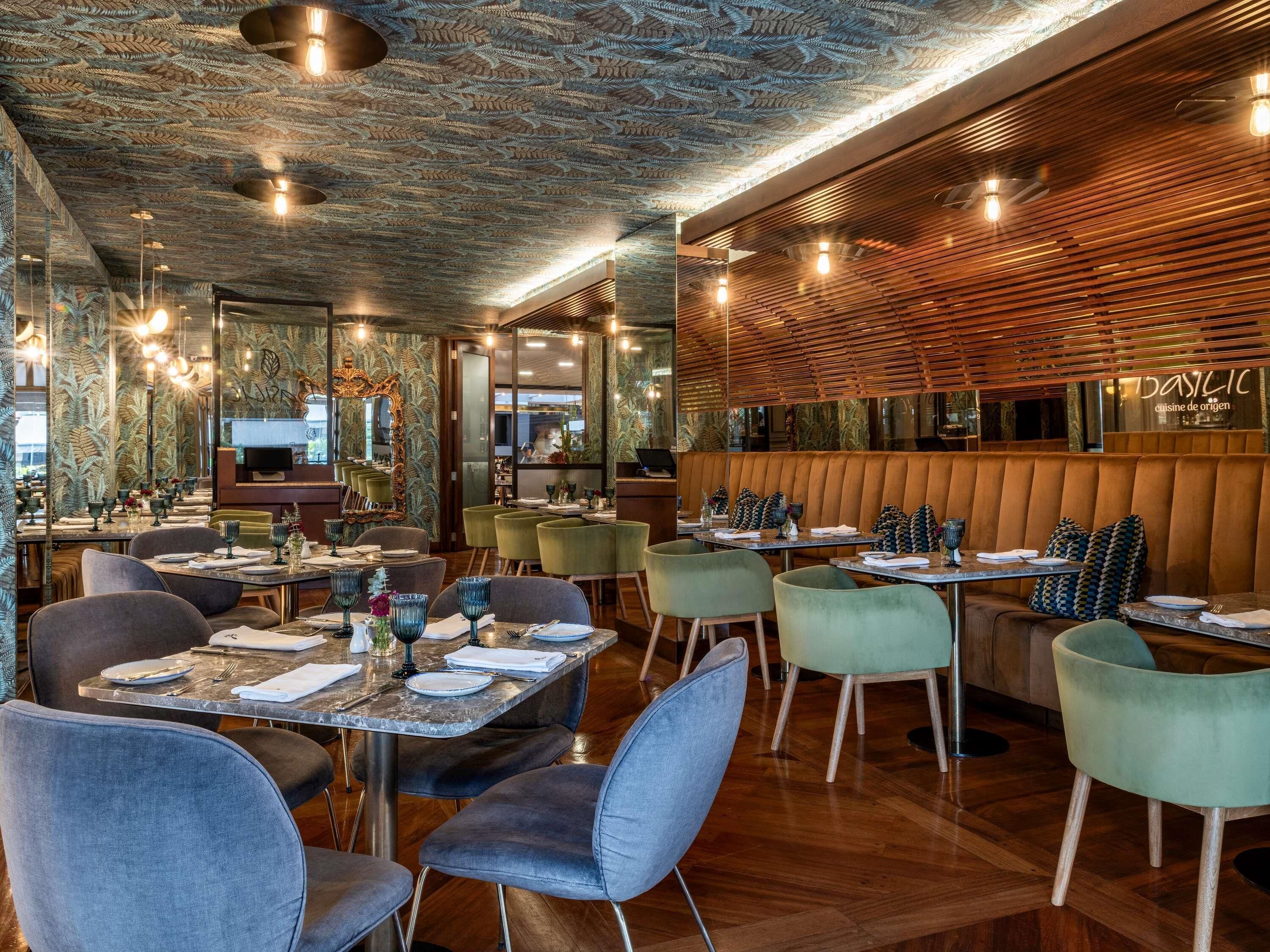 En restaurantindretning med et mønstret loft, væg af trælameller og grønne polstrede stole.