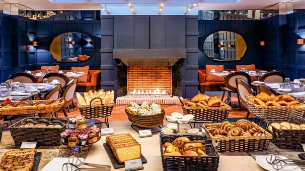 A modern dining area with a central fireplace, multiple seating arrangements, and a variety of food displays. - Sofitel Bogota Victoria Regia (Bogotá)