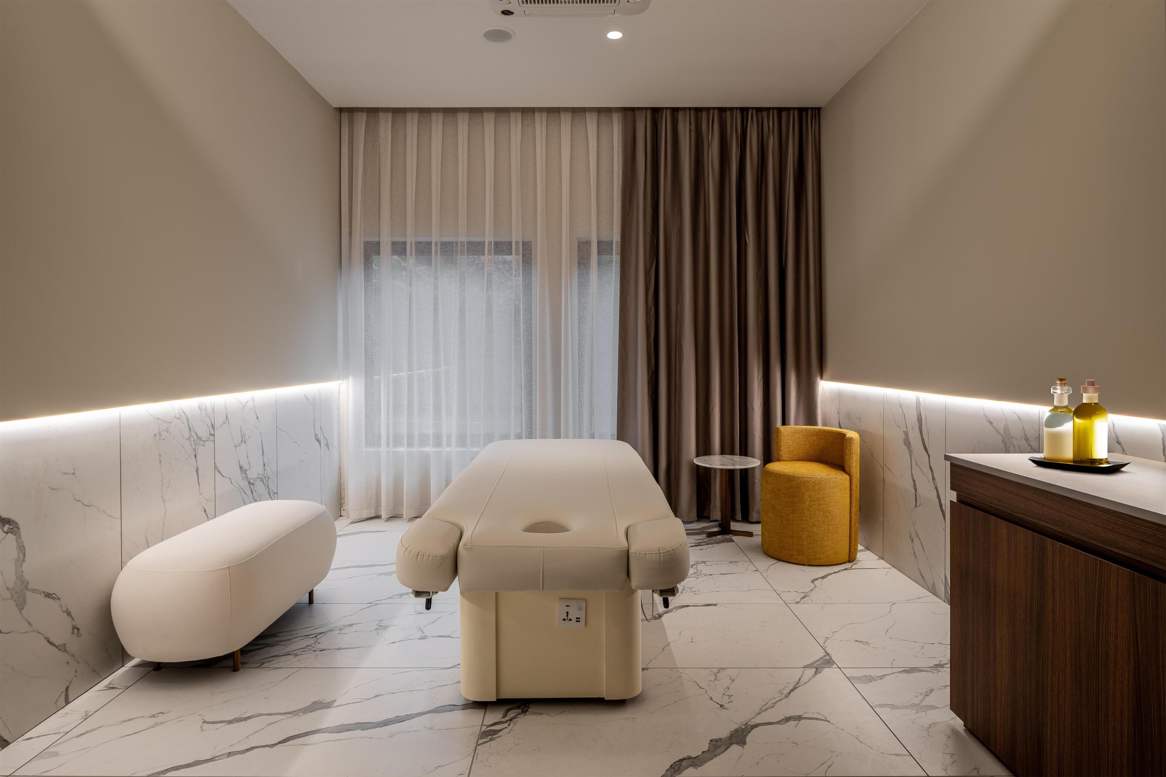 A modern bathroom with a massage chair, a small round table, and a vanity with bottles.