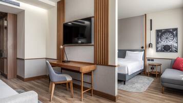 A modern hotel room with a wooden desk, a bed, a grey sofa, and a small round table.