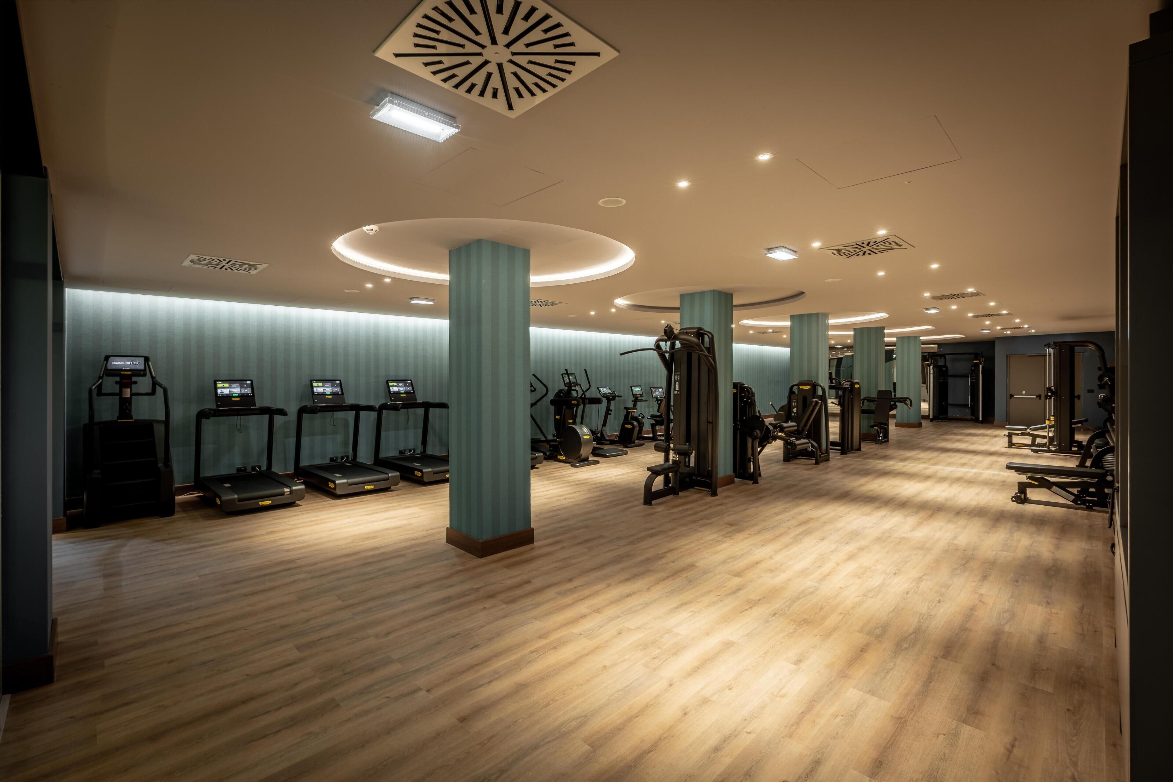 Un gimnasio espacioso con numerosas cintas de correr, elípticas y equipo de levantamiento de pesas.