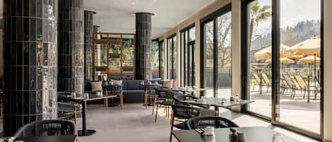 A modern restaurant with high ceilings, large windows, and a view of outdoor seating.