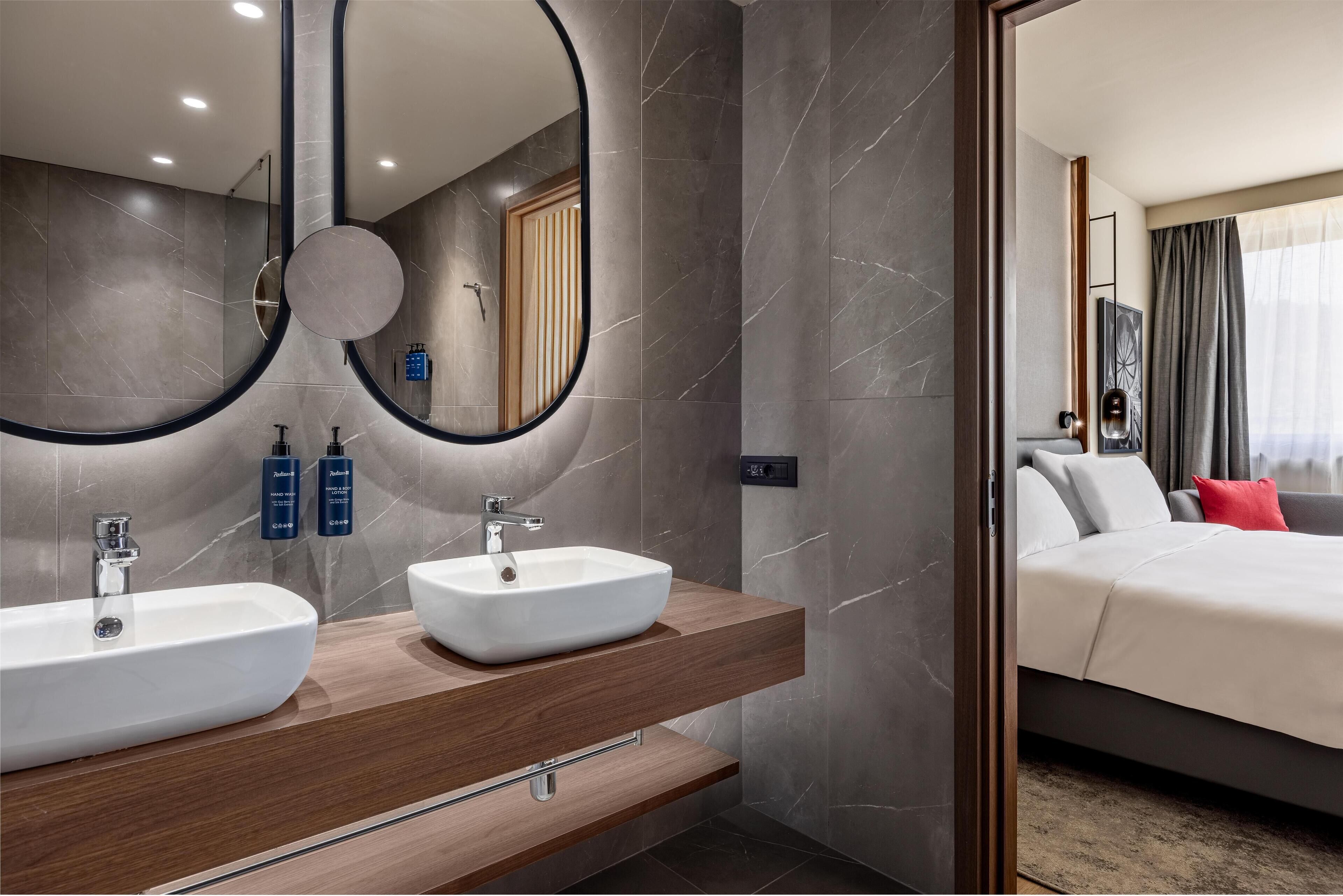 Een moderne badkamer met twee wastafels, een grote spiegel en een houten wastafelmeubel.