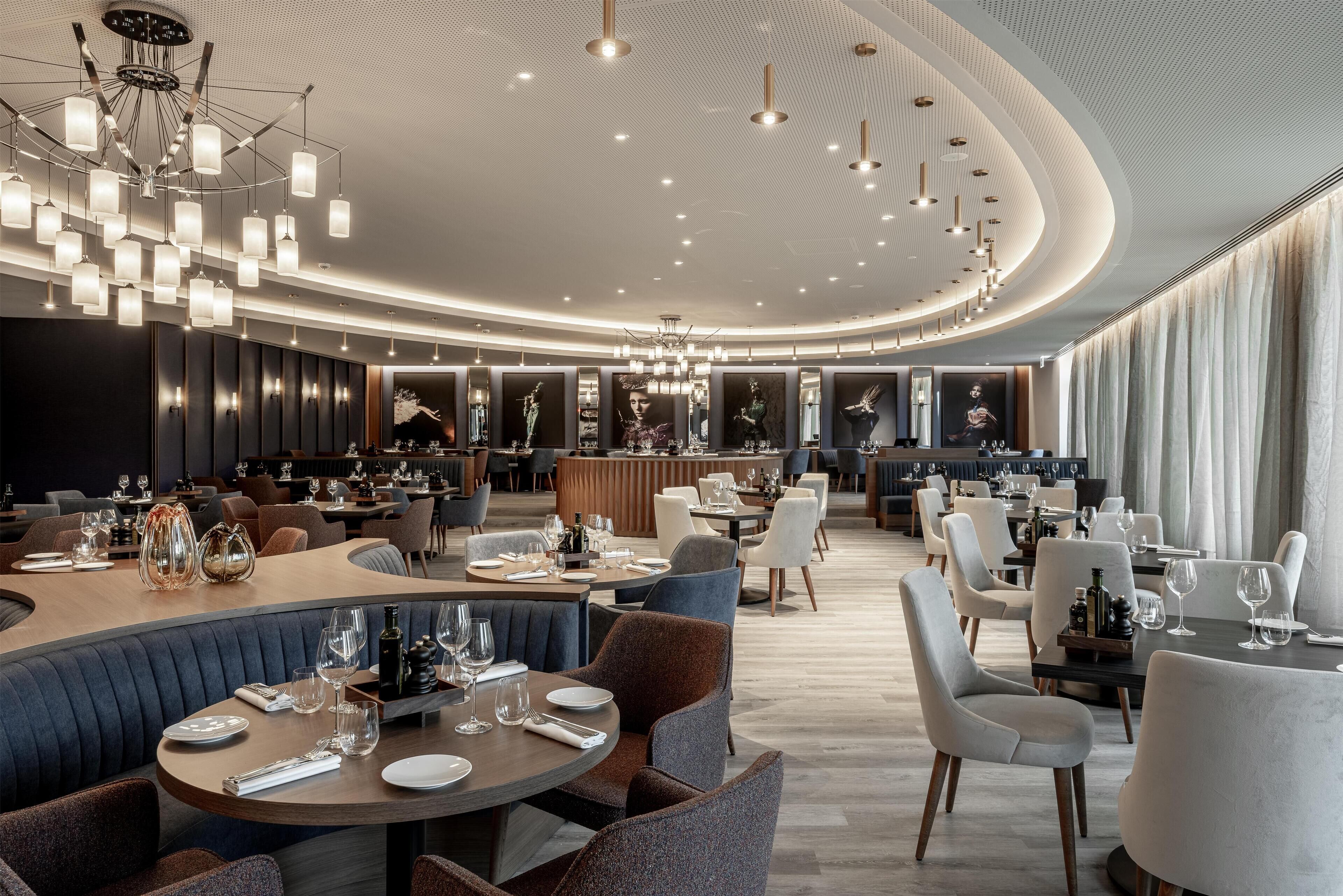 A modern restaurant with round tables, comfortable seating, and a stylish ceiling design.