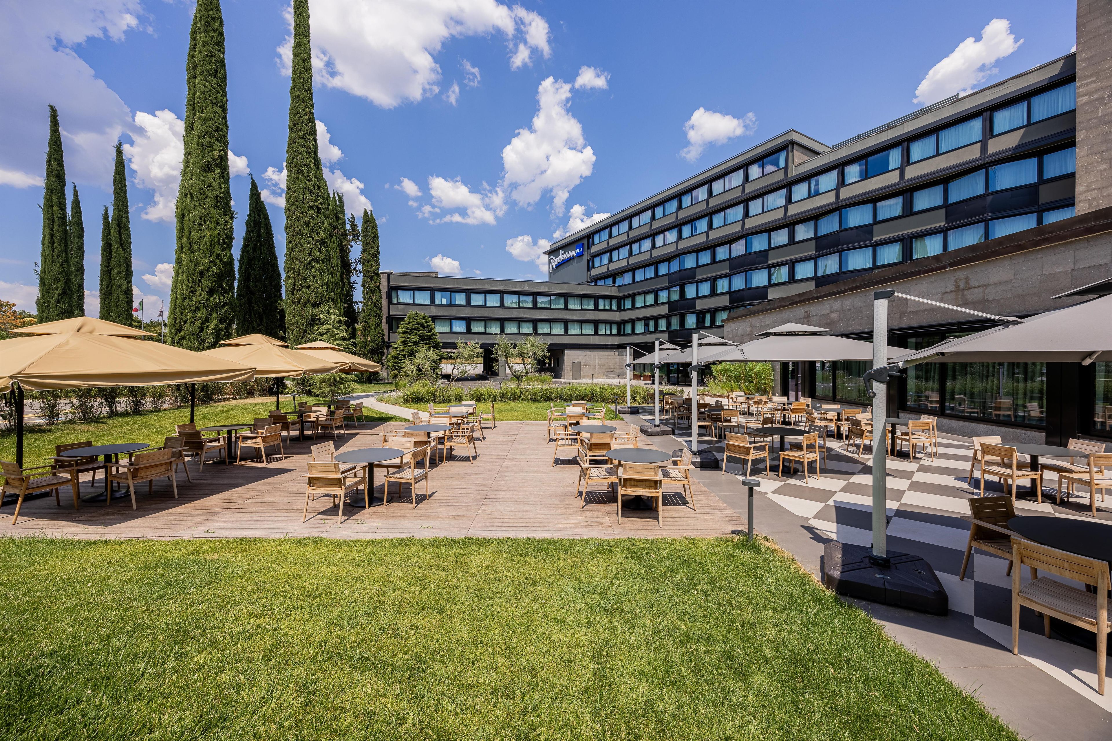 Une cour d’hôtel avec des espaces de repos en plein air, une pelouse et de grands arbres.