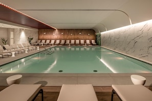 Une piscine intérieure moderne, dotée de chaises longues et d’un mur en bois.