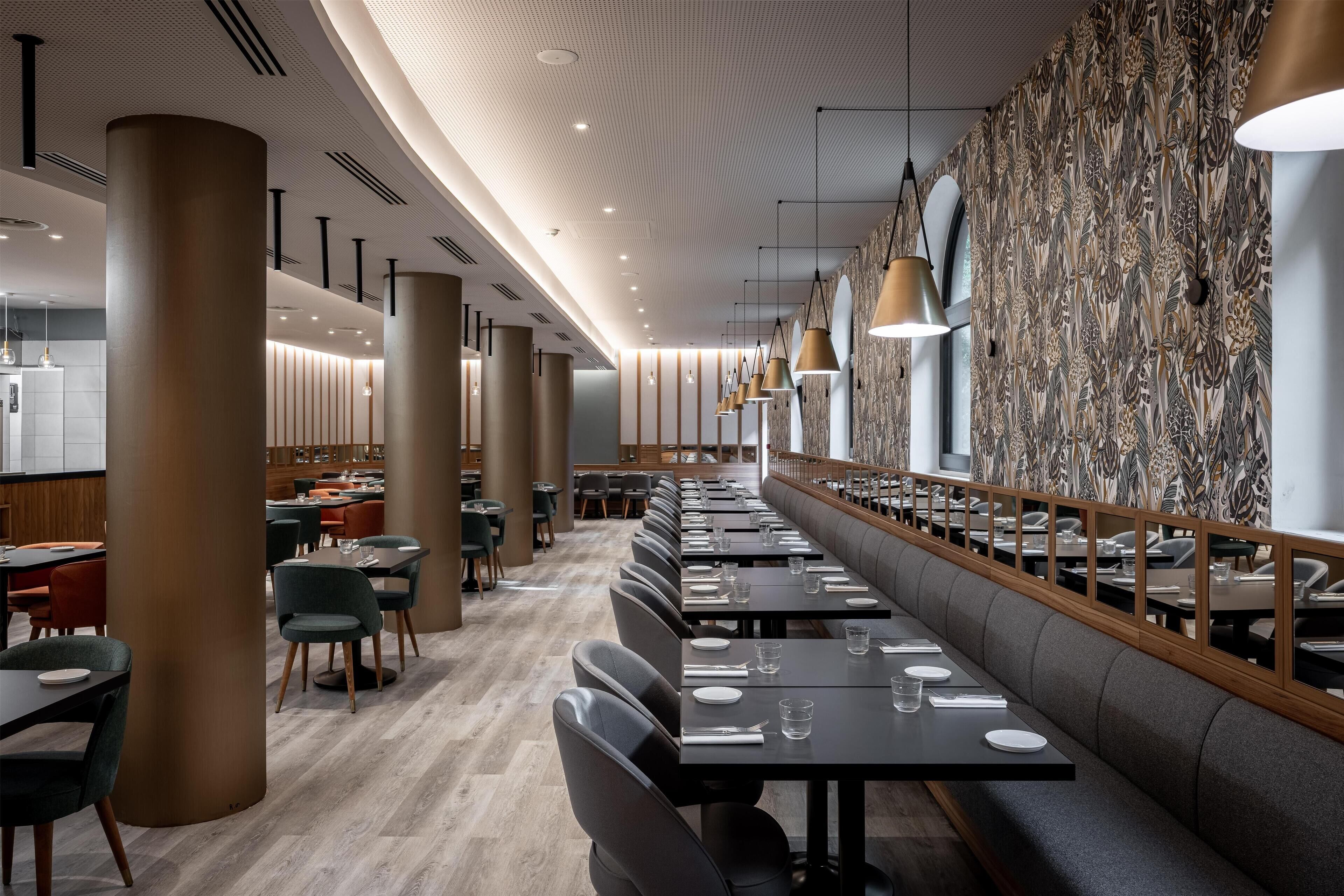 A modern restaurant with a long counter, high ceiling, and patterned wallpaper.