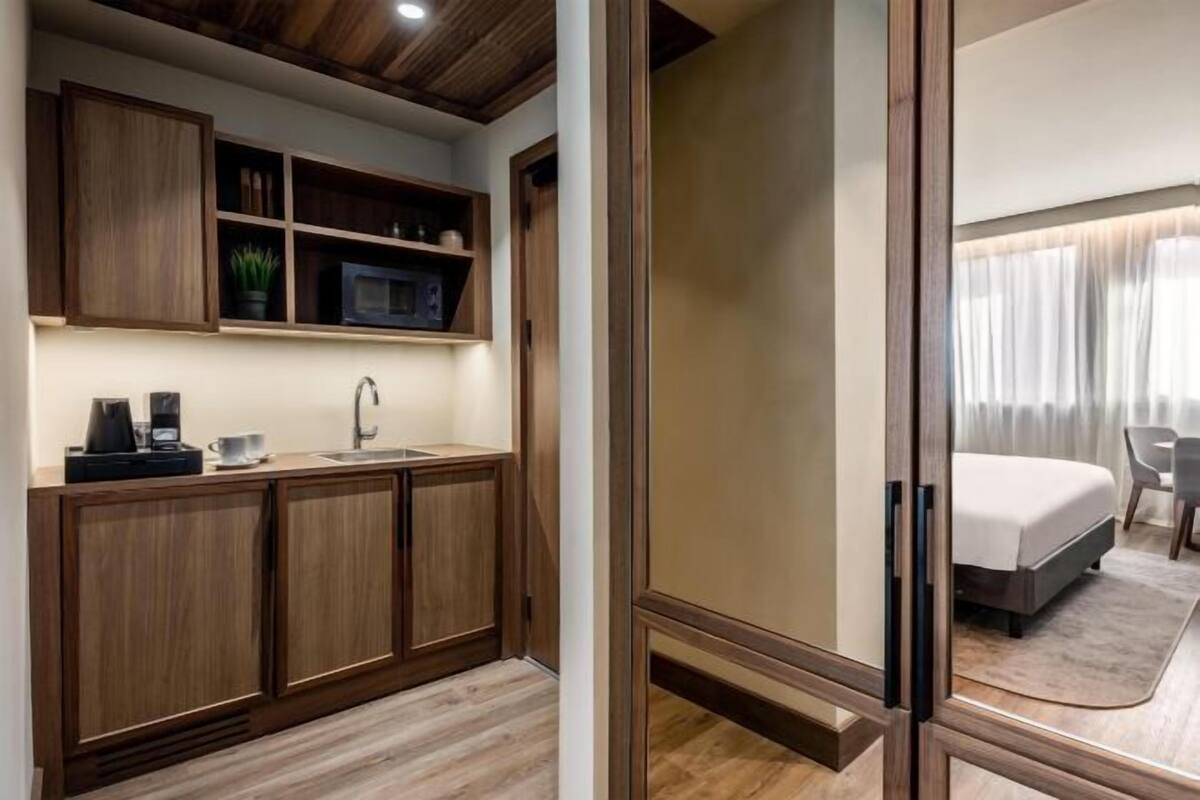 Une chambre d’hôtel compacte, dotée d’une kitchenette, d’un lit et offrant une vue sur l’extérieur.