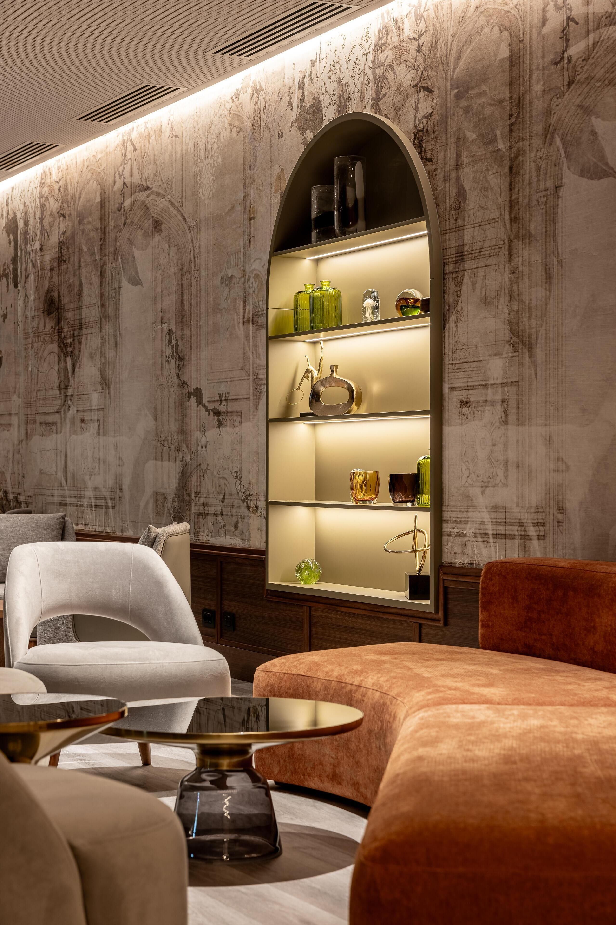 Ein modernes Interieur mit Marmorwand, einer eingebauten Vitrine mit Dekoration, einem weißen Sessel und einem runden Tisch.