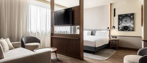 A modern hotel room with a sofa, armchairs, a TV, a bed, and a small table.