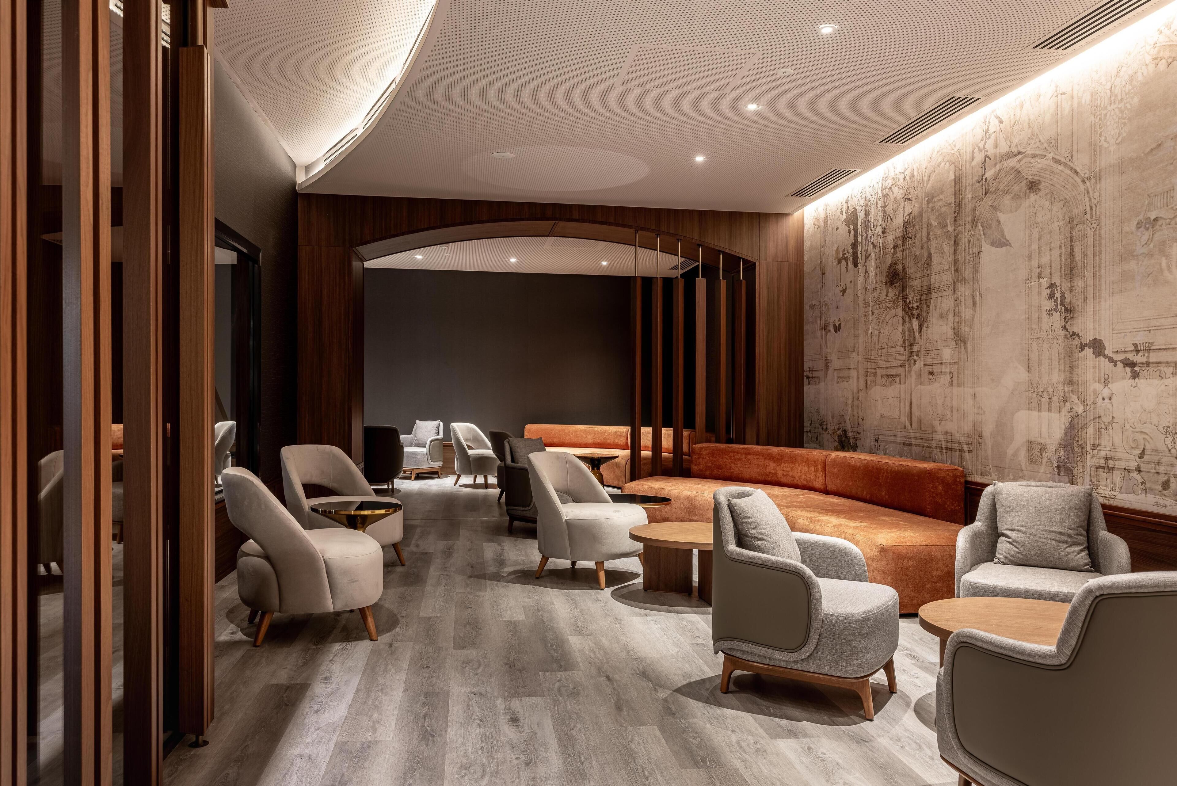 Et moderne loungeområde med sofaer, lænestole og et sofabord, med en træafskærmning og et vægmaleri.