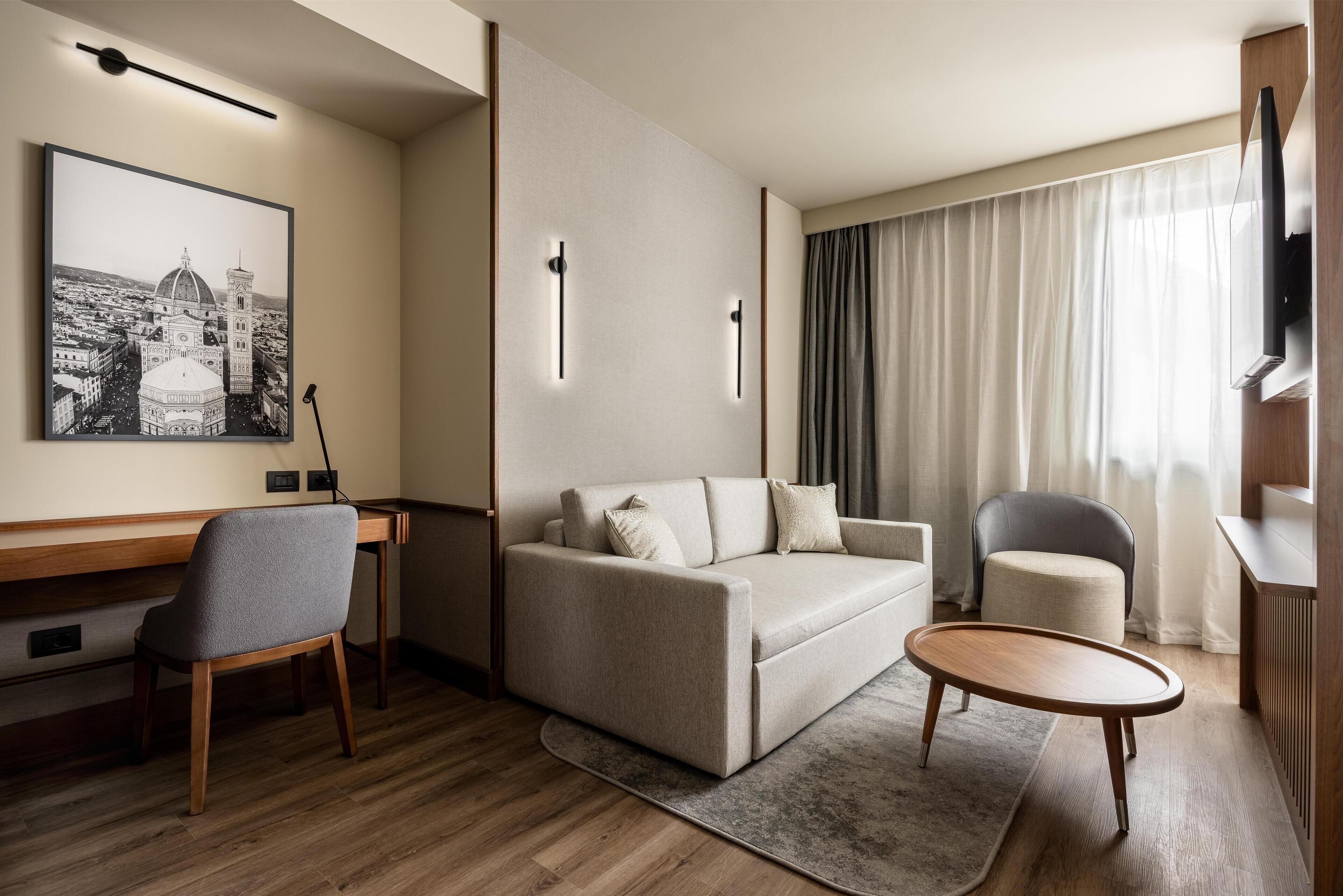 Una sala de estar moderna con un sofá, dos sillones, una mesa de centro, un televisor de pantalla plana, un cuadro de un paisaje urbano y un escritorio de madera.