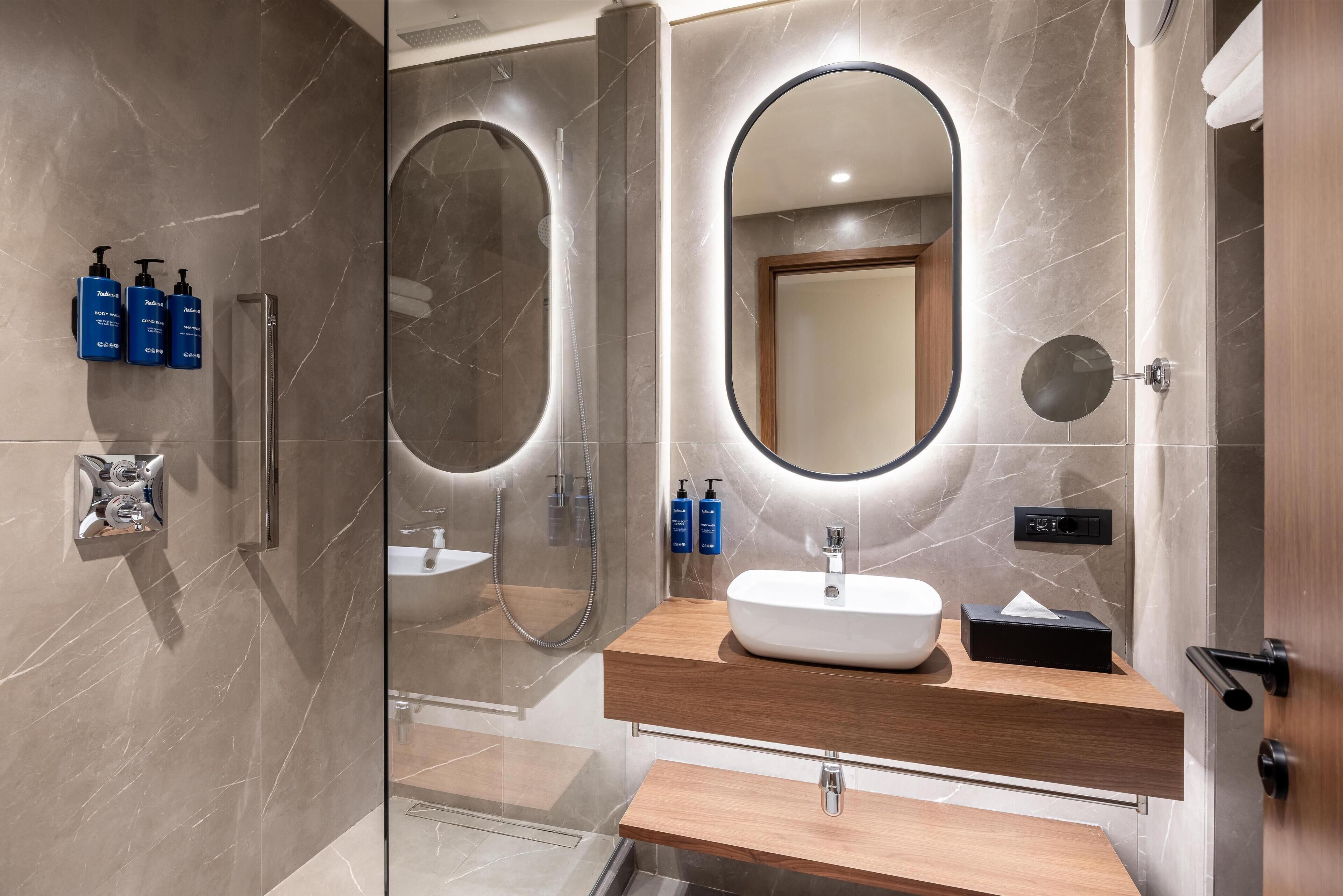 A modern bathroom with a glass-enclosed shower, a wooden vanity with a sink, and a large mirror.