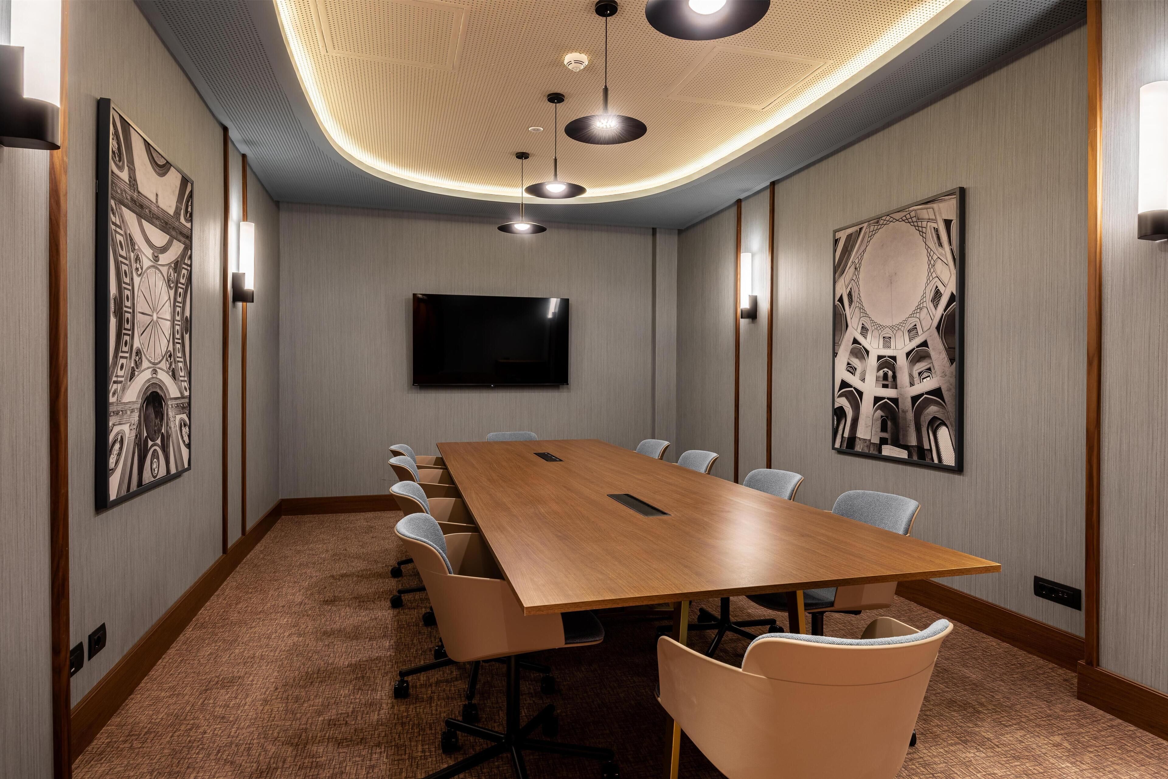 A conference room with a long table, chairs, a flat-screen TV, and artwork on the walls.