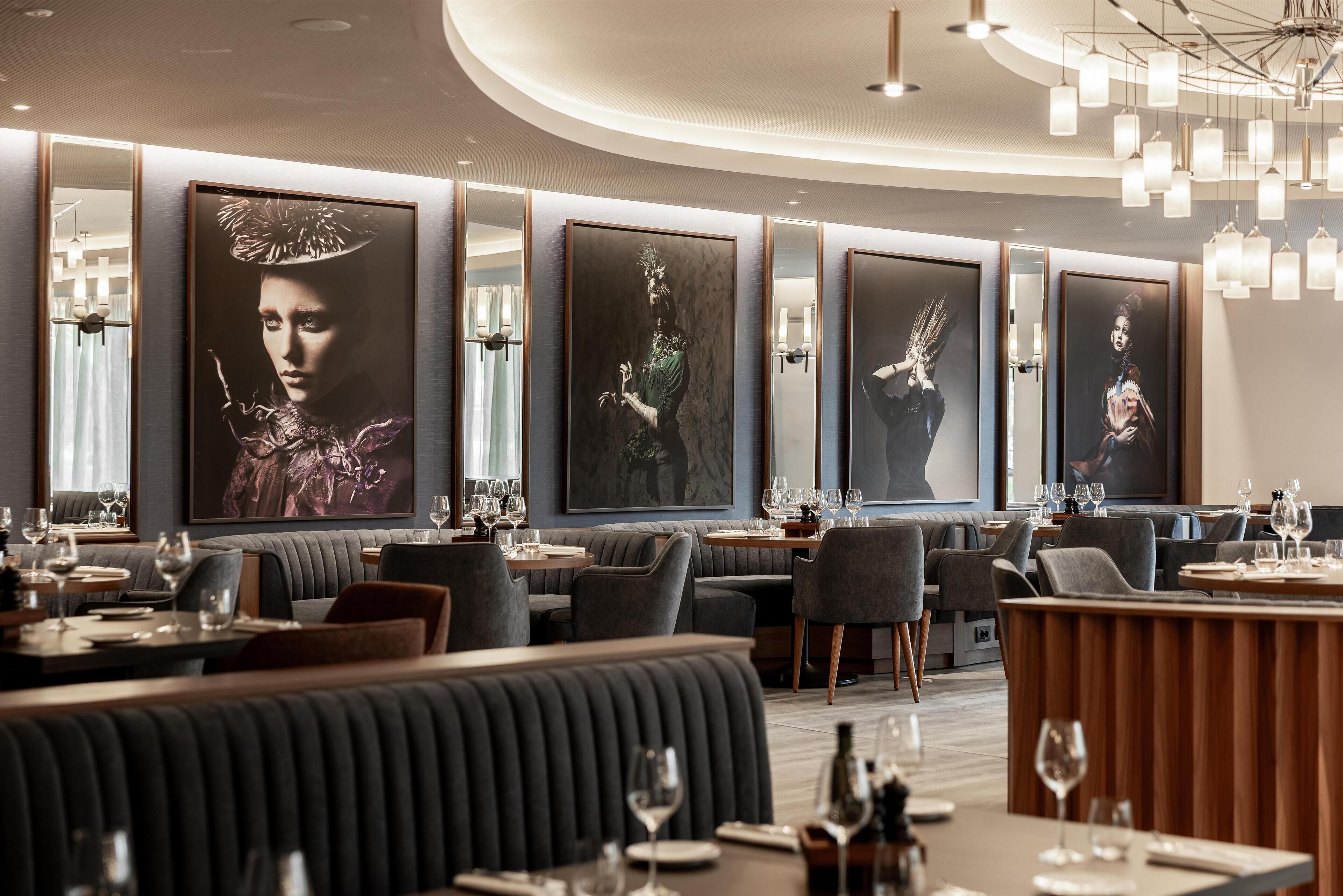 Un restaurant moderne avec des banquettes à haut dossier, des tables rectangulaires et un bar central.