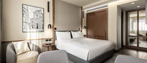A modern hotel room with a large bed, a seating area with a round table, and a framed artwork on the wall.
