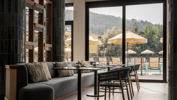 Un área de estar moderna con sofá, mesa de comedor, sillas y vistas a sombrillas exteriores y una piscina.