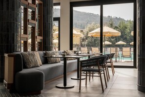 A modern lounge area with a sofa, dining table, chairs, and a view of outdoor umbrellas and a pool. - Radisson Blu Hotel, Florence (Florence)
