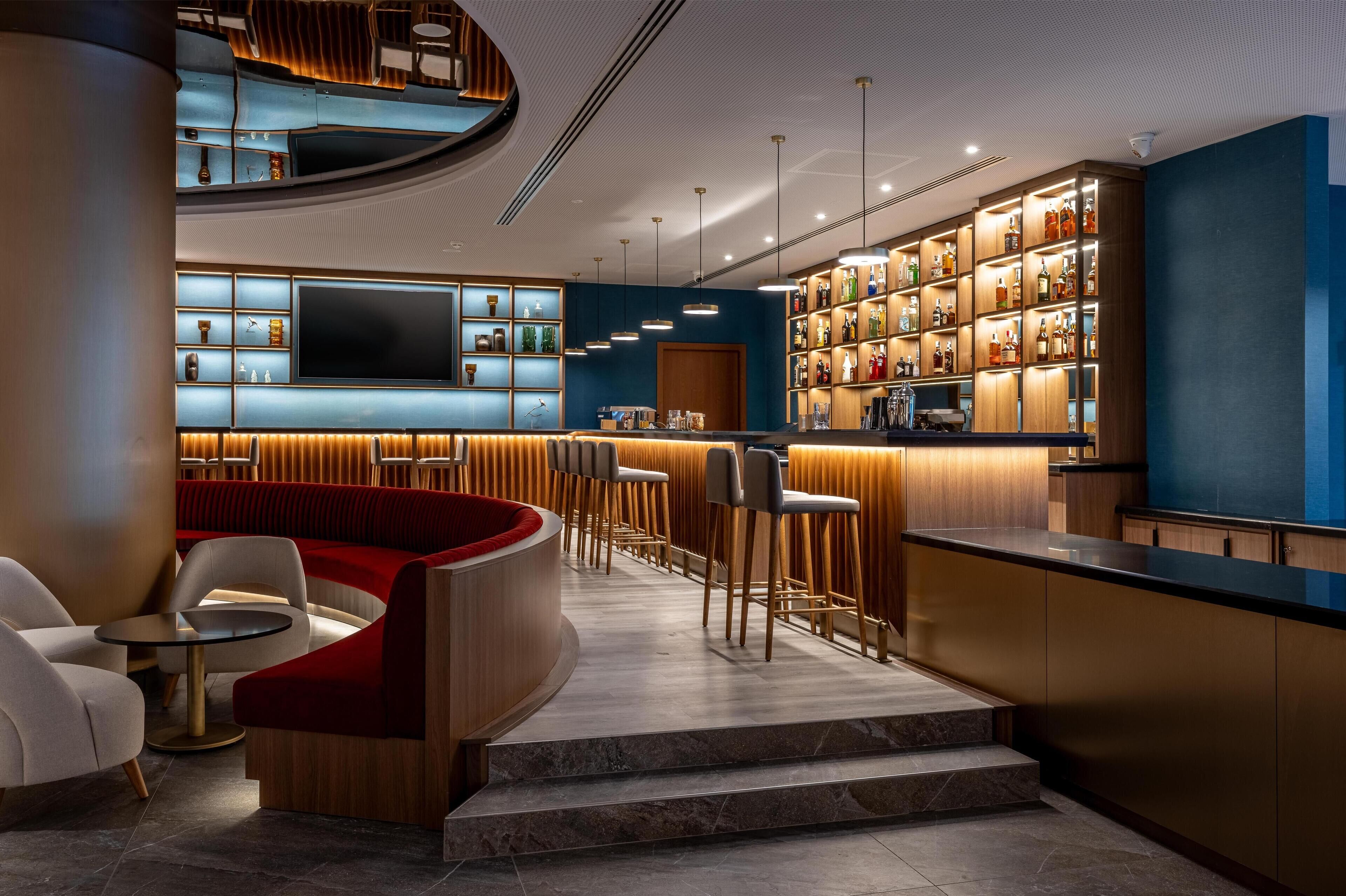 A modern bar area with seating, a TV, and a well-lit liquor display.