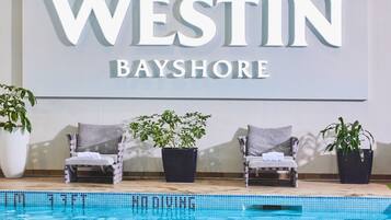 Zona junto a la piscina con sillones de descanso y plantas en macetas, un cartel que dice 'WESTIN BAYSHORE' y una piscina azul cristalina.