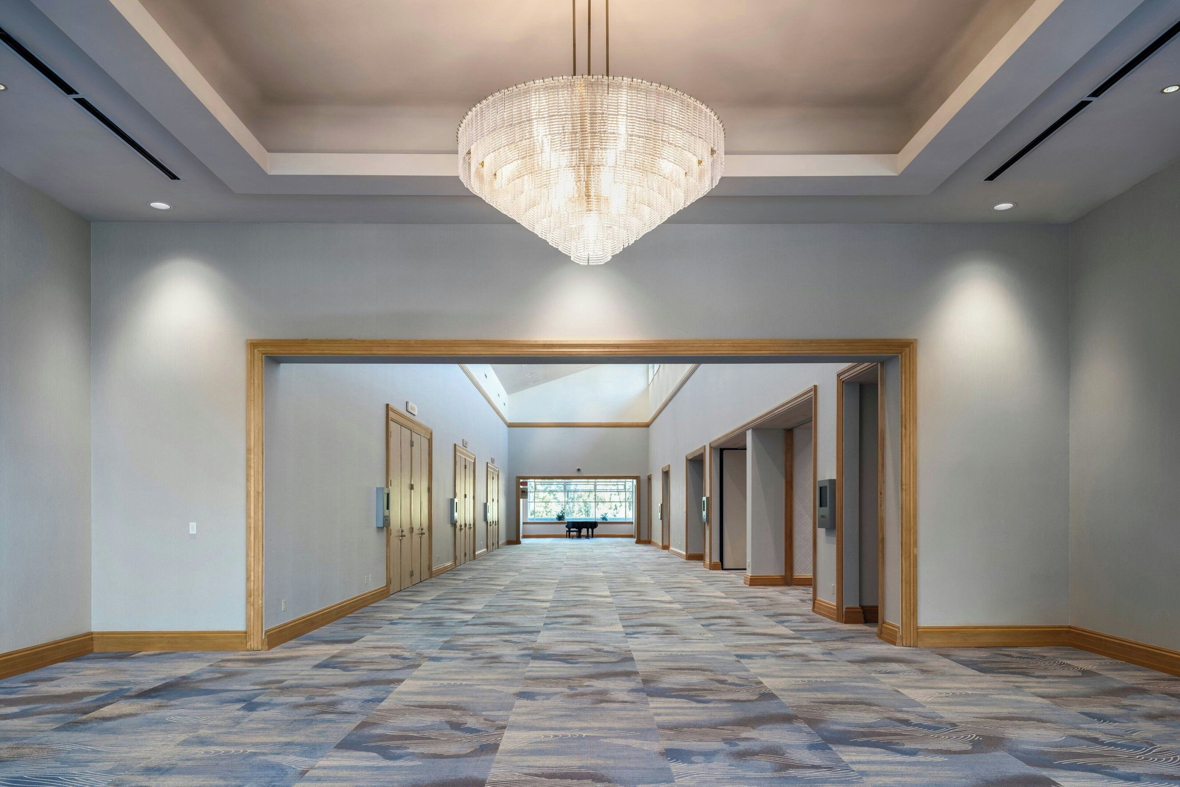 A spacious hallway with a patterned floor, a large chandelier, and doors leading to rooms.