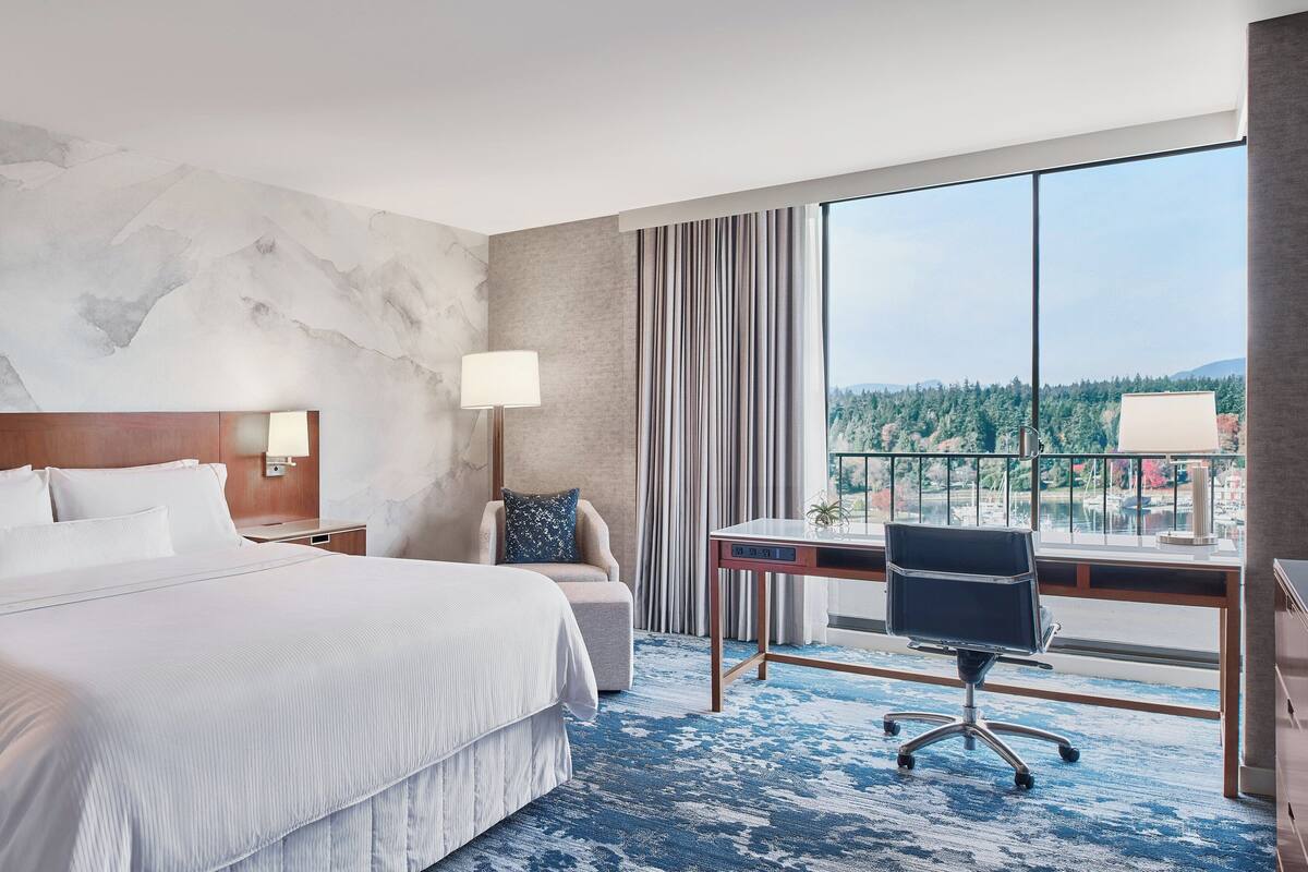 A hotel room with a large bed, a desk, and a view of a cityscape.
