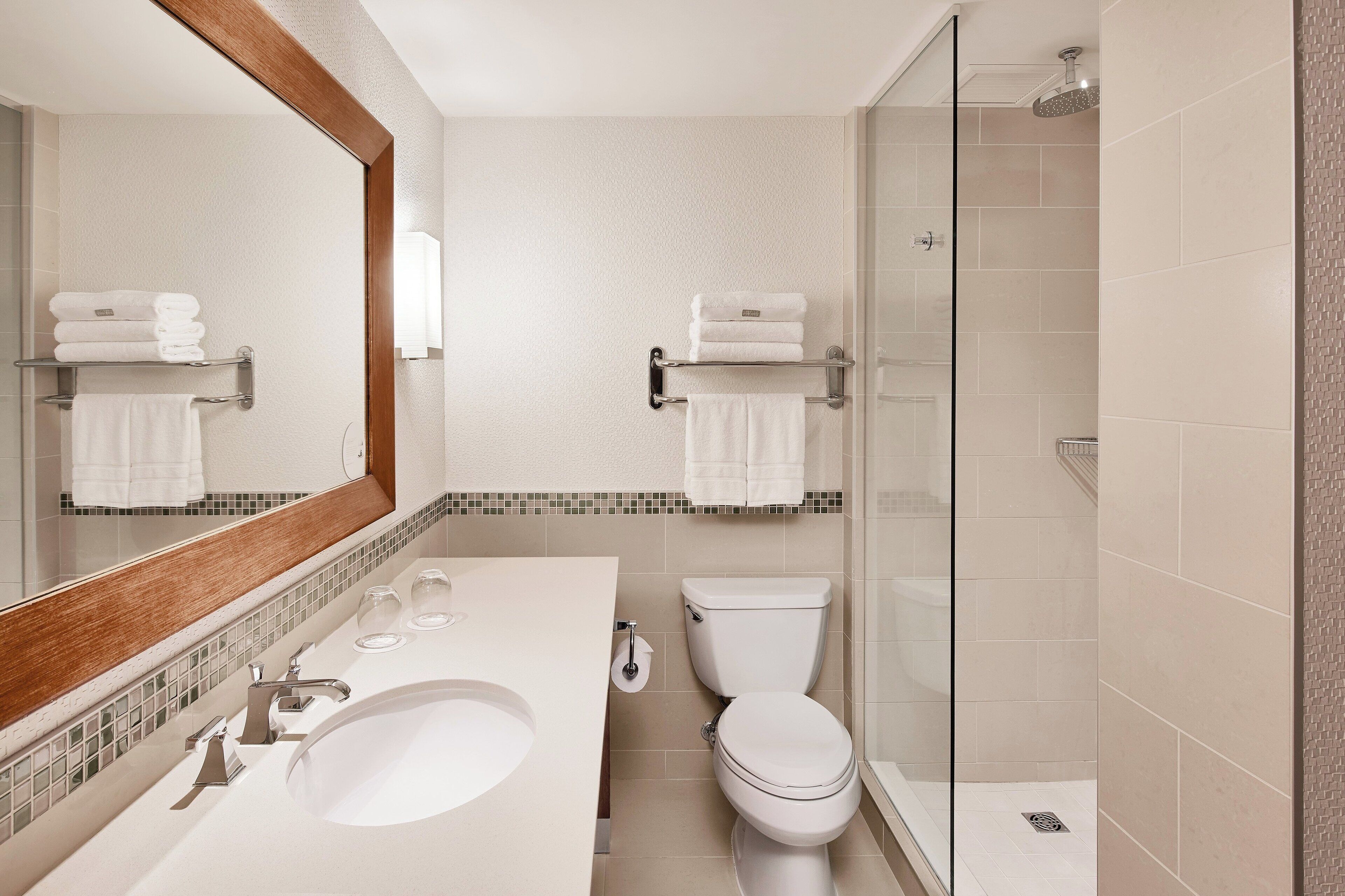 A modern bathroom with a large mirror, a sink, a toilet, and a glass-enclosed shower.
