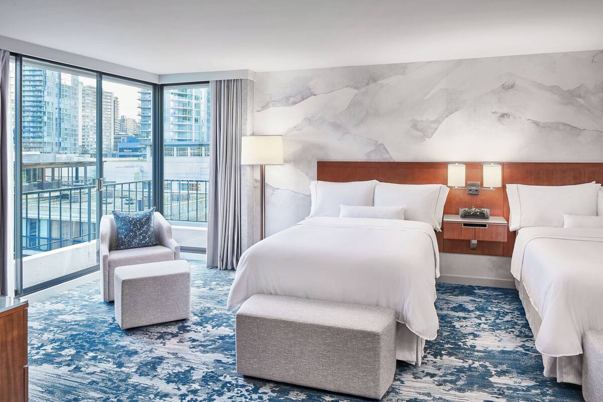 A hotel room with a large window, a bed, a chair, and a small table.