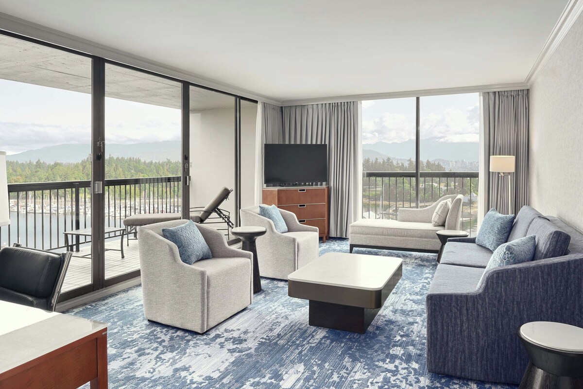 A spacious living room with a large TV, comfortable seating, and a balcony with a scenic view.