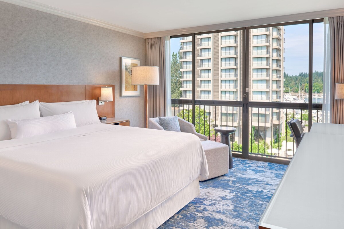 A hotel room with a large bed, a desk, and a view of a high-rise building.